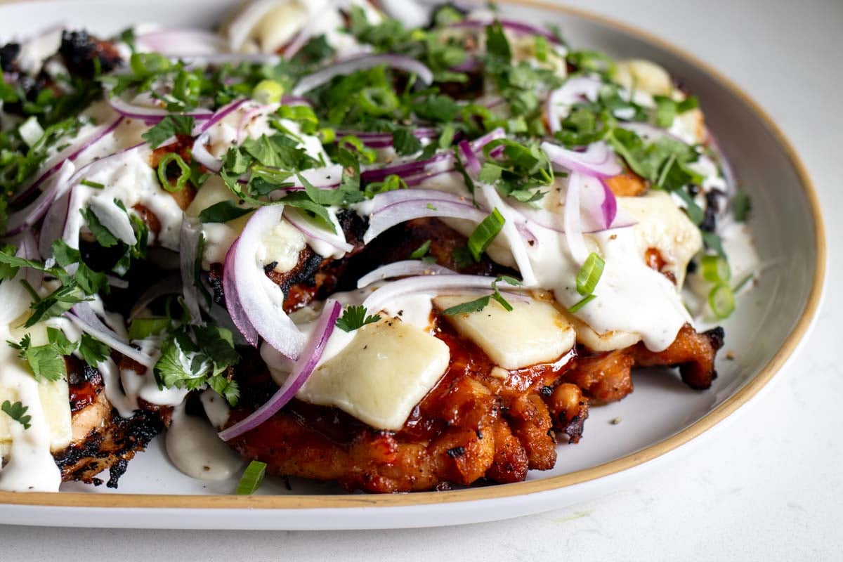a white plate full of golden red bbq chicken topped with melted cheddar, onion, cilantro and scallions.