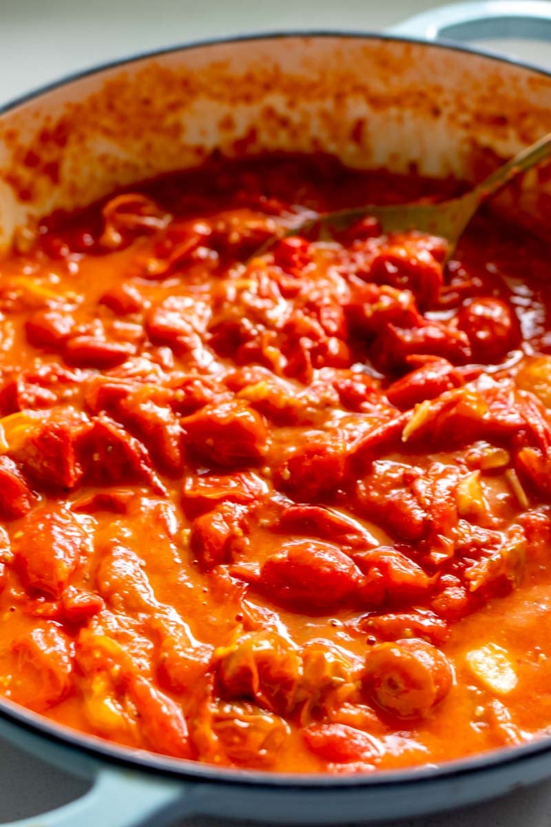 A blue braiser full of bright red burst tomatoes with a light sauce around it.