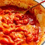 a pot with bright red burst tomatoes in it and a golden spoon.