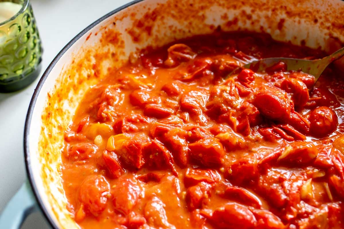 A blue braiser full of bright red burst tomatoes with a light sauce around it.