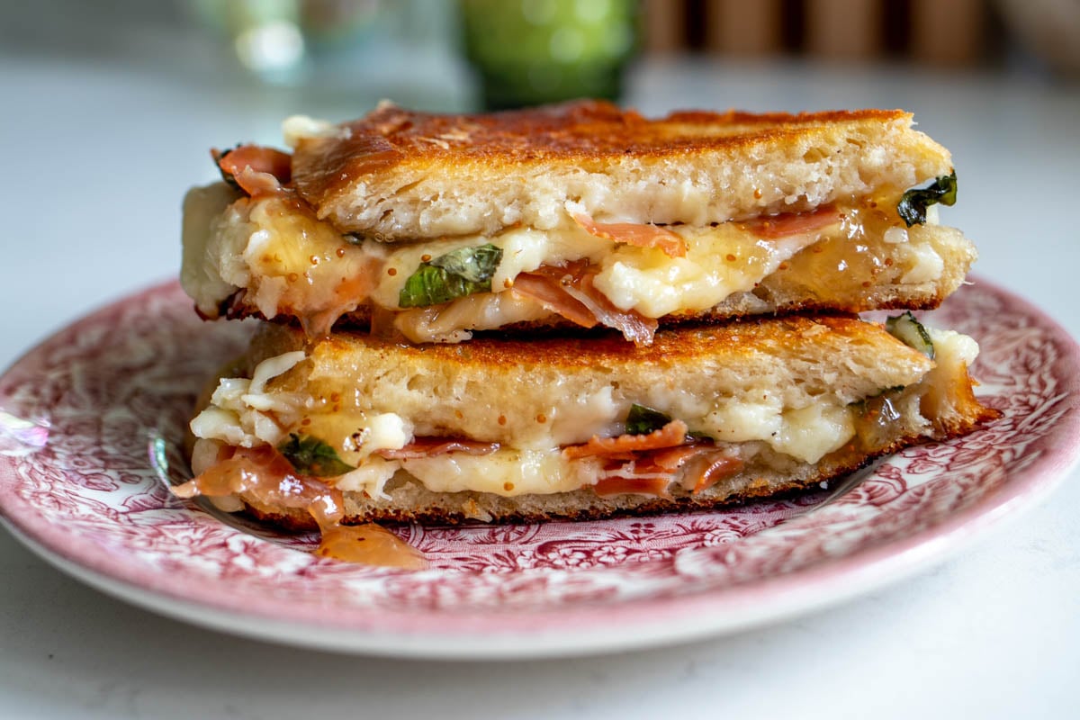 a gourmet grilled cheese on a antique plate on a white table top.