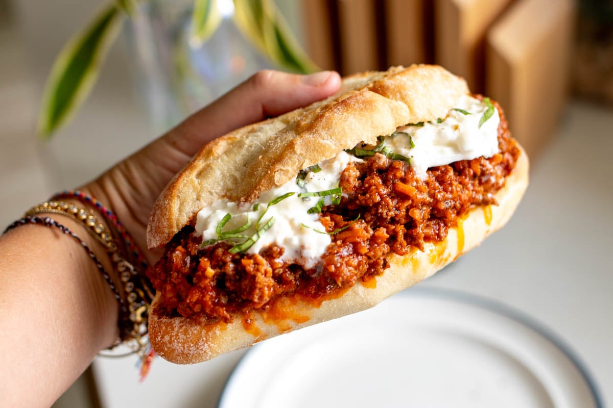 a hand holding a massive italian sloppy joe with bits of burrata dripping off.