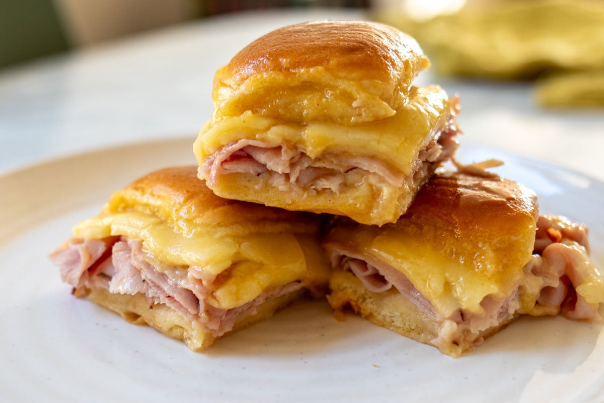 a white plate topped with 3 ham nad cheese sliders with cheese oozing out.