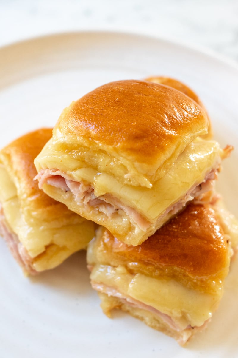 a few ham and cheese sliders on a white plate with a golden glaze.