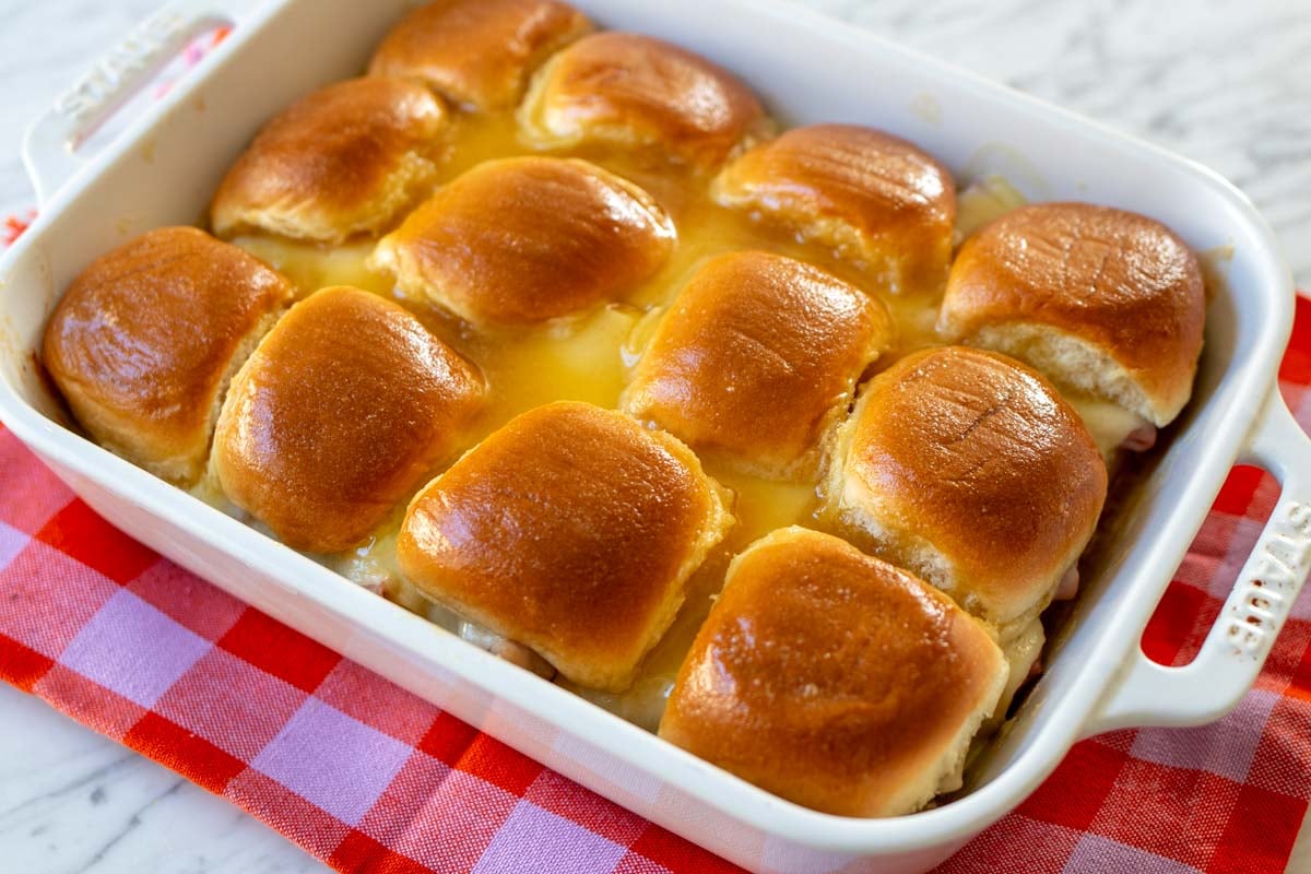 a baking dish full of hawaiian roll sliders on a marble countertop with a bright colored napkin.