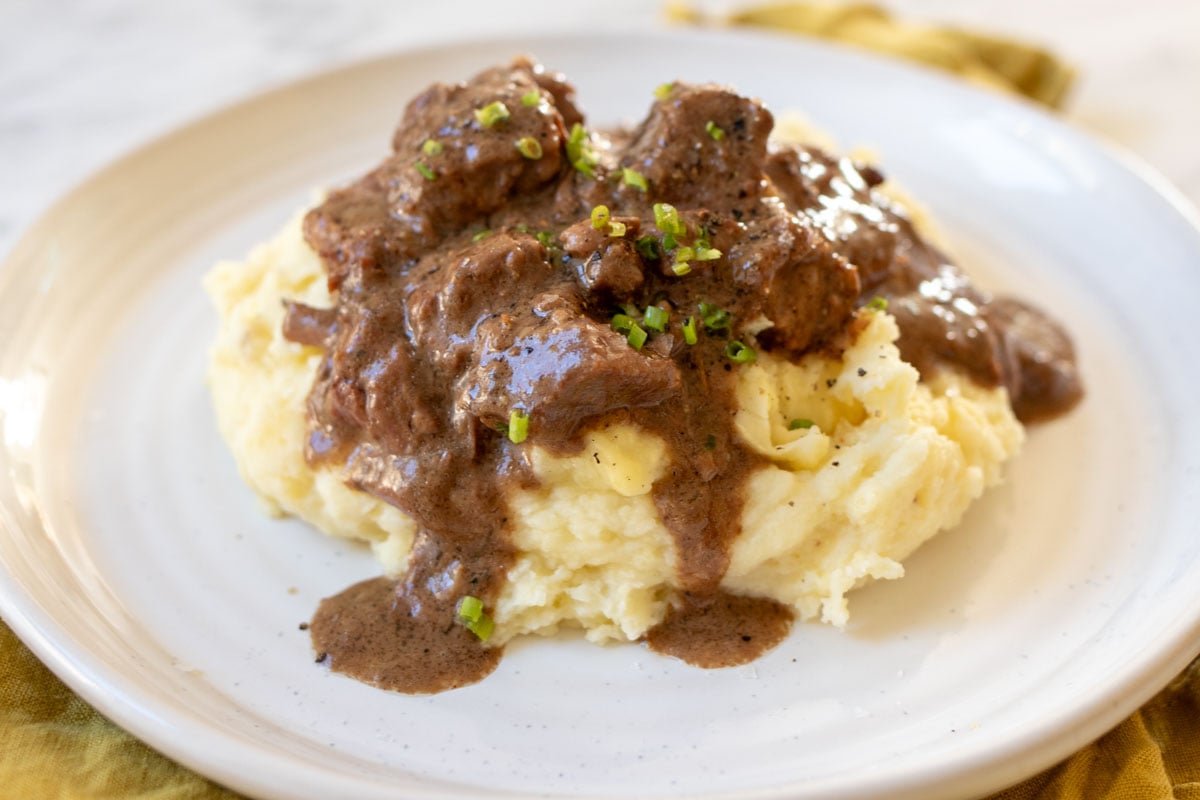 a beautiful plate full of mashed potatoes and steak bites in a creamy peppercorn sauce.