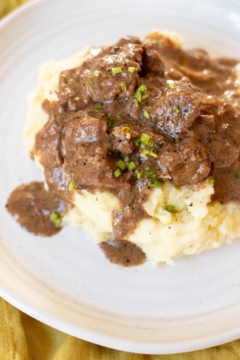 steak bites in an au poivre sauce over mashed potatoes on a white plate.