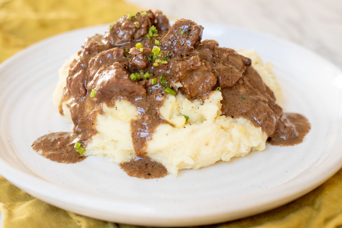 a pile of boursin mashed potatoes topped with steak bites au poivre that are made in the slow cooker.