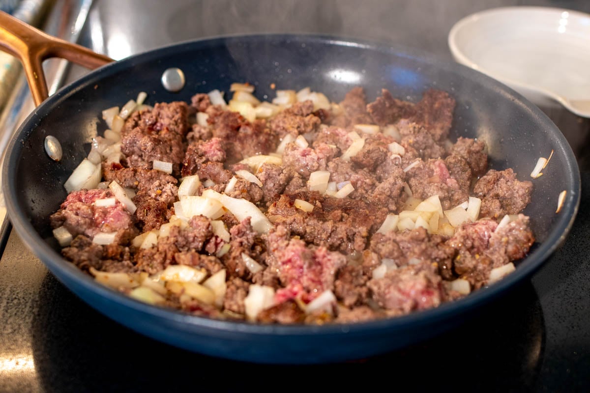 a frying pan cooking up ground beef with onions and sauce.