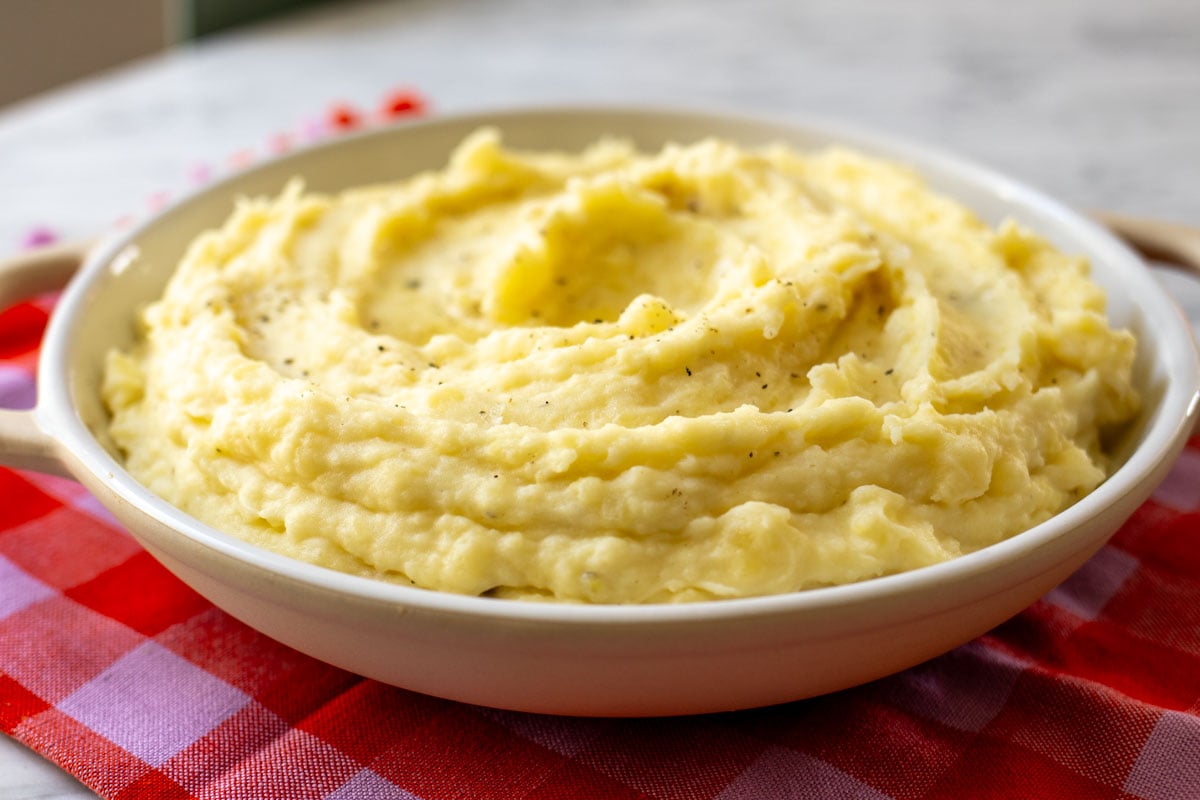 a side profile of a white bowl filled with creamy mashed potatoes with boursin cheese.