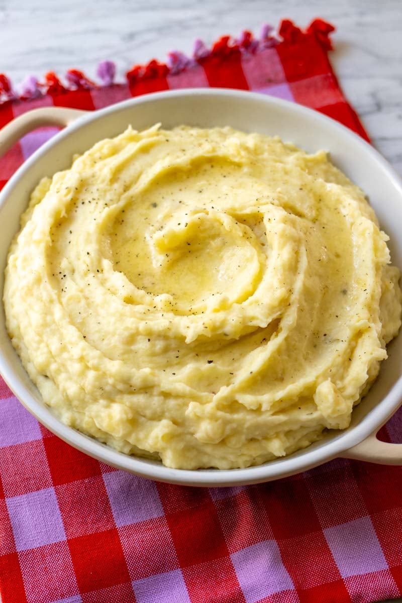 a pink napkin topped with a white serving bowl full of garlic and herb mashed potatoes.