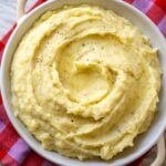 a white dish full of creamy mashed potatoes that are swirled with boursin cheese.
