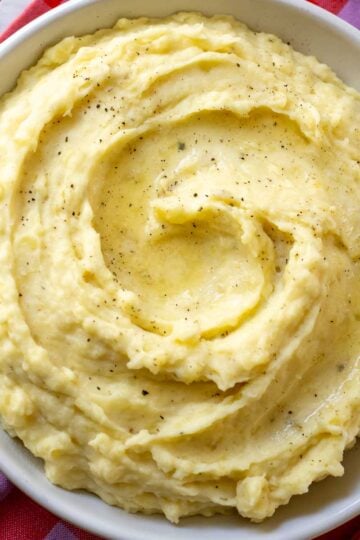 a white dish full of creamy mashed potatoes that are swirled with boursin cheese.