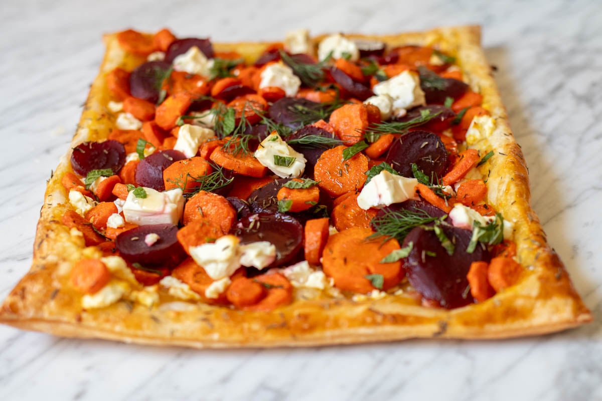 a birds eye view of this carrot tart with chunks of feta, pickled beets, and green herbs on a marble surface.