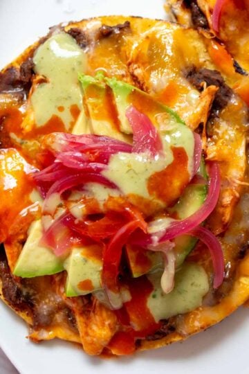 a bright and colorful chicken tostada with green salsa and pink pickled onions on a white plate.