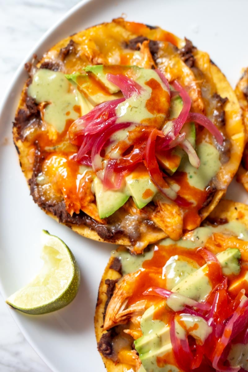 a white plate full of colorful chicken tostadas with black beans.
