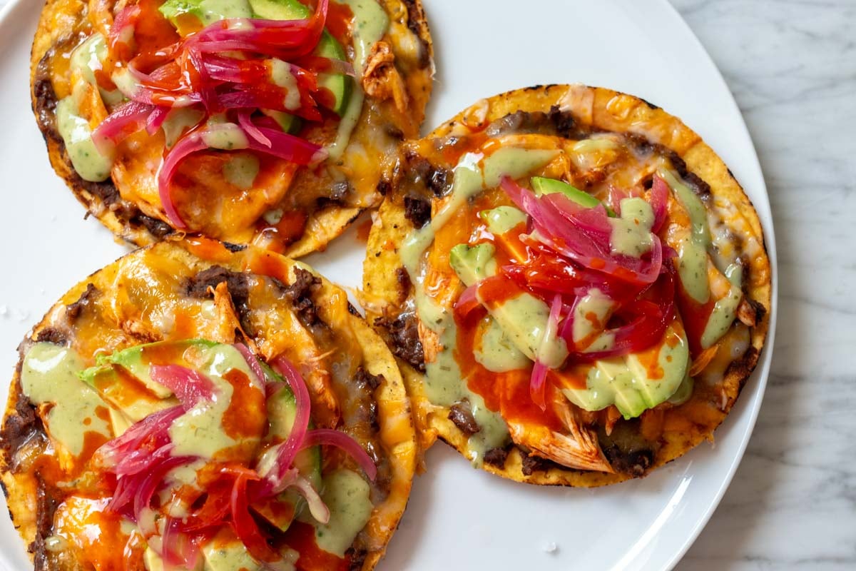 a white plate full of cheesy chicken tostadas on a marble countertop.