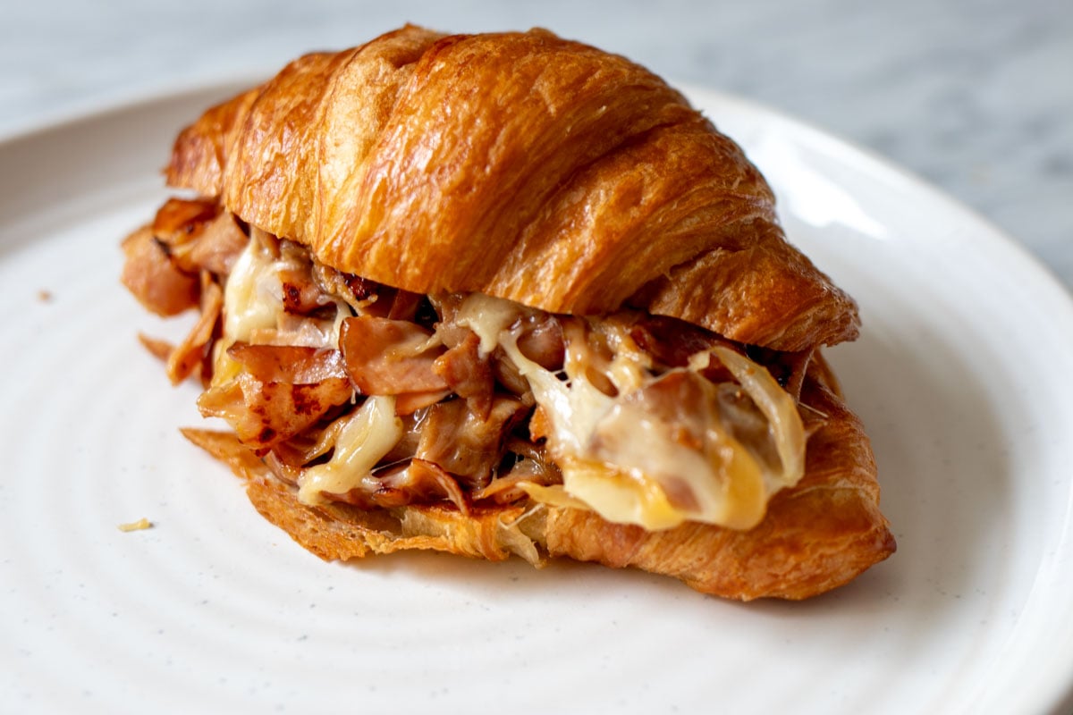 a beautiful ham and cheese croissant on a white plate.