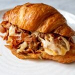 a chopped ham and cheese croissant on a white plate with oozing cheese.