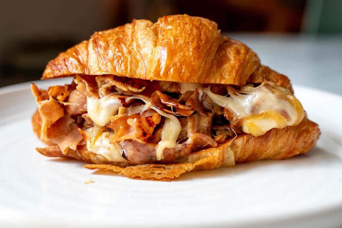 a chopped ham and cheese mixture stuffed into a golden brown croissant on a white plate.
