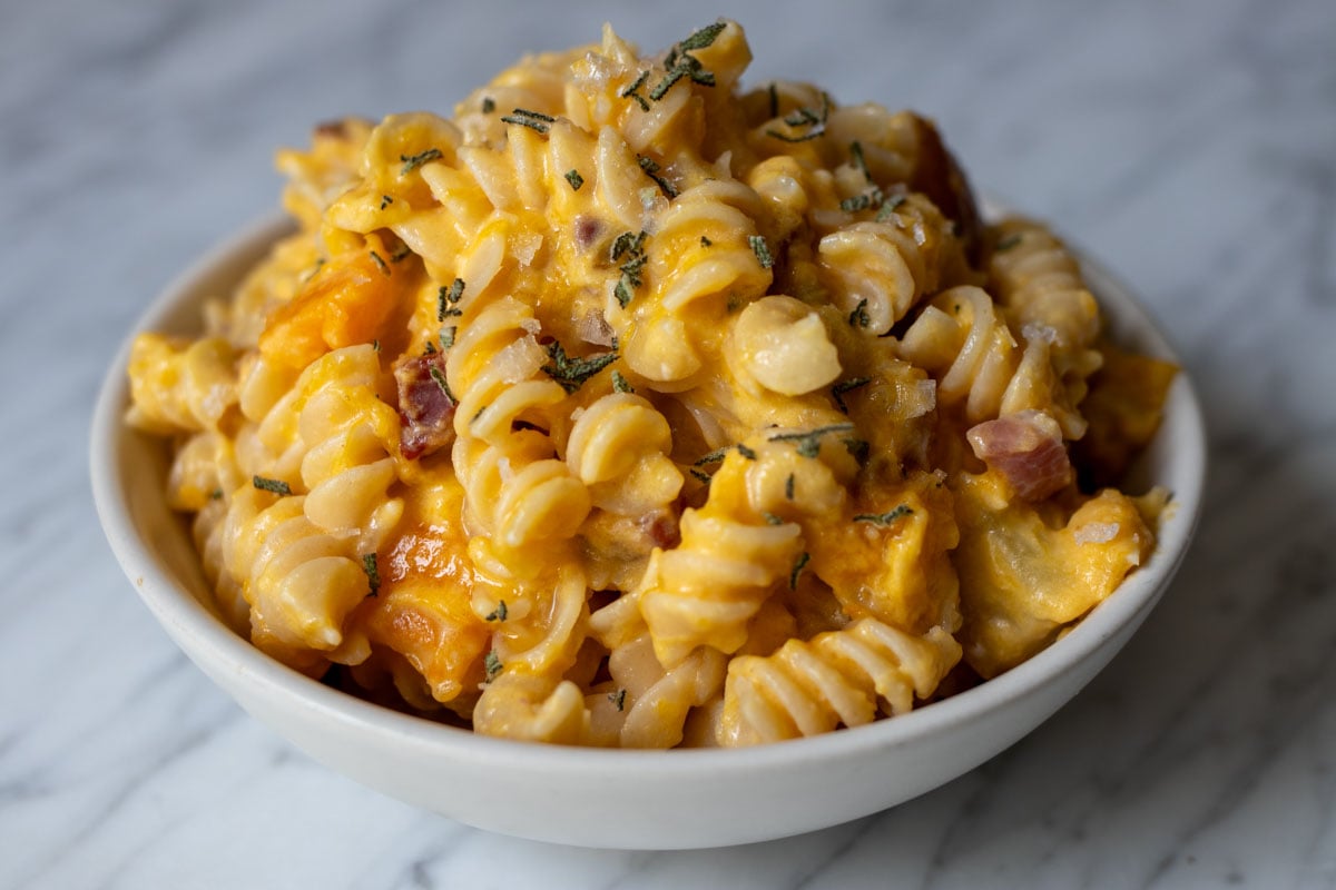 a white bowl full of goat cheese pasta with butternut squash, pancetta, sage and garlic.
