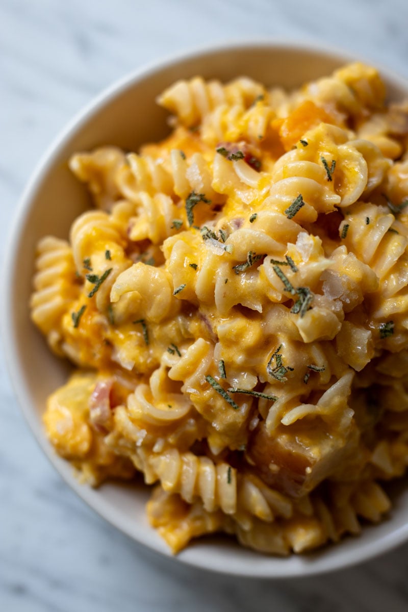 an overhead view of a bowl of goat cheese pasta with butternut squash on a marble countertop.