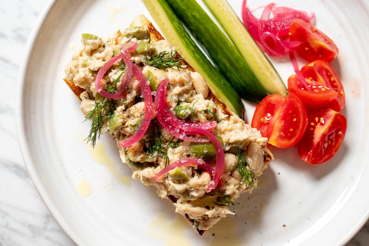 a piece of grilled ciabatta topped with lemony tuna salad on a white plate with the chopped veggies to the side.