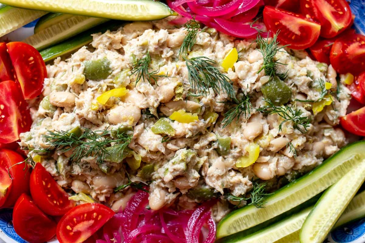 a close up of a platter full of tuna salad with bits of olive, dill and banana peppers surrouned by colorful chopped veggies.
