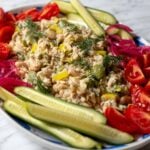 a white plate full of tuna salad that's seasoned with lemon and olives and dill then paired with cucumbers, tomatoes and pickled red onions.