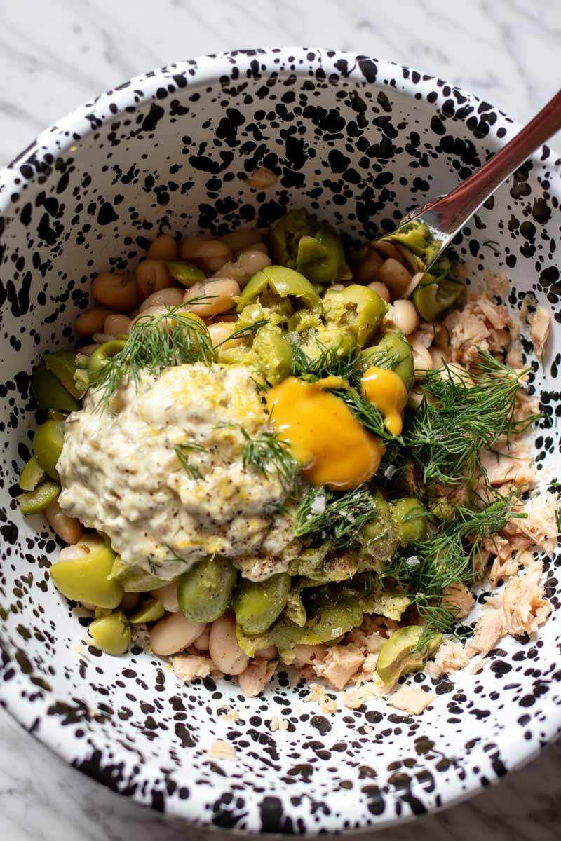 all of the ingredients that are needed to make this lemony tuna salad in a speckled black and white bowl.