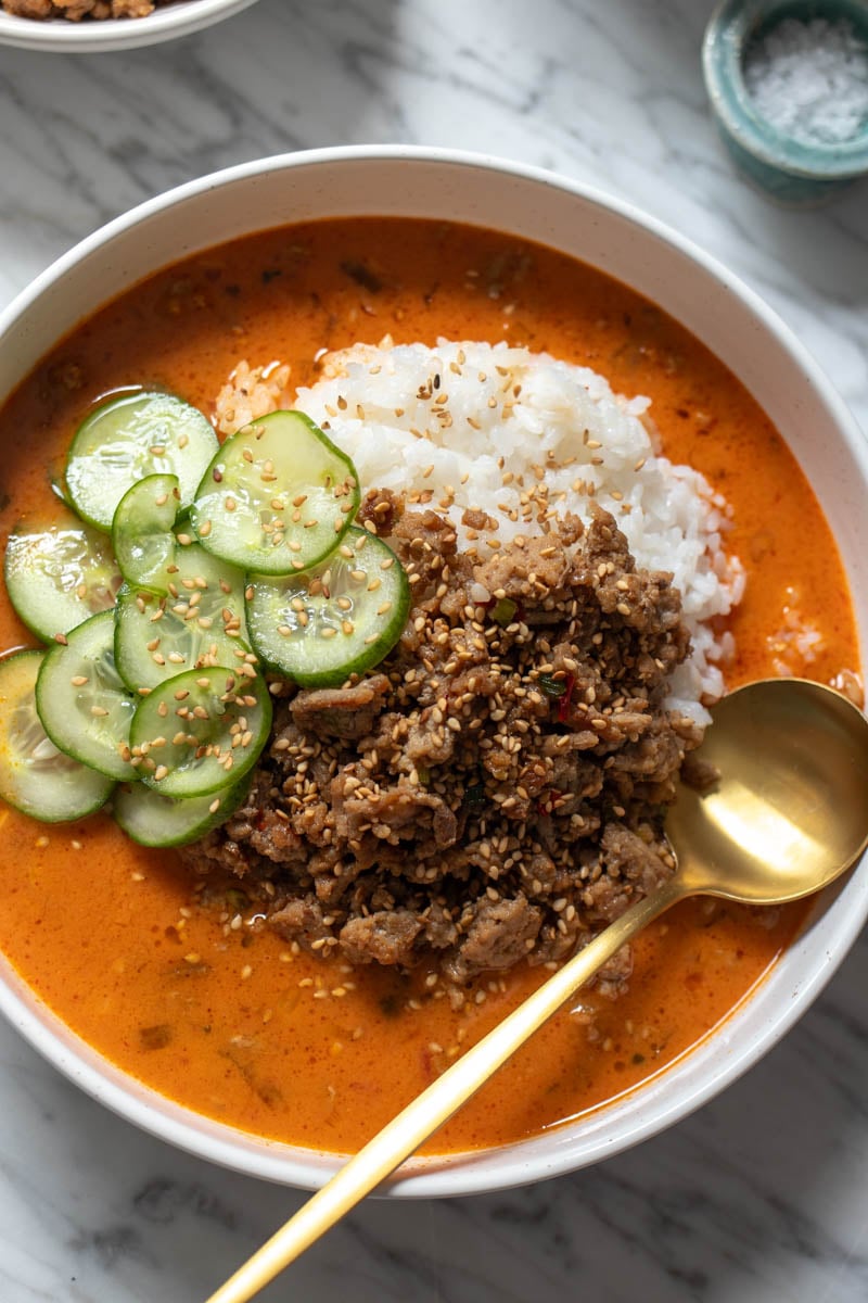an overhead view of a broth bowl in a white bowl with a golden spoon on a marble countertop.