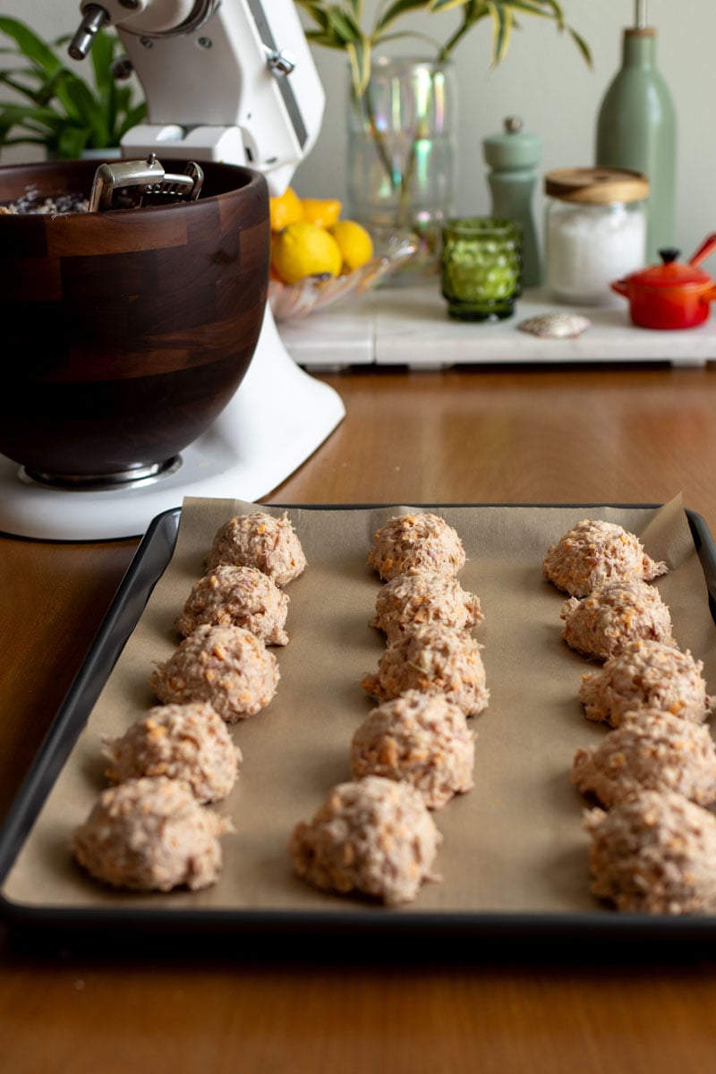 cheddar apple sausage balls being formed on a baking sheet with a stand mixer in the background.