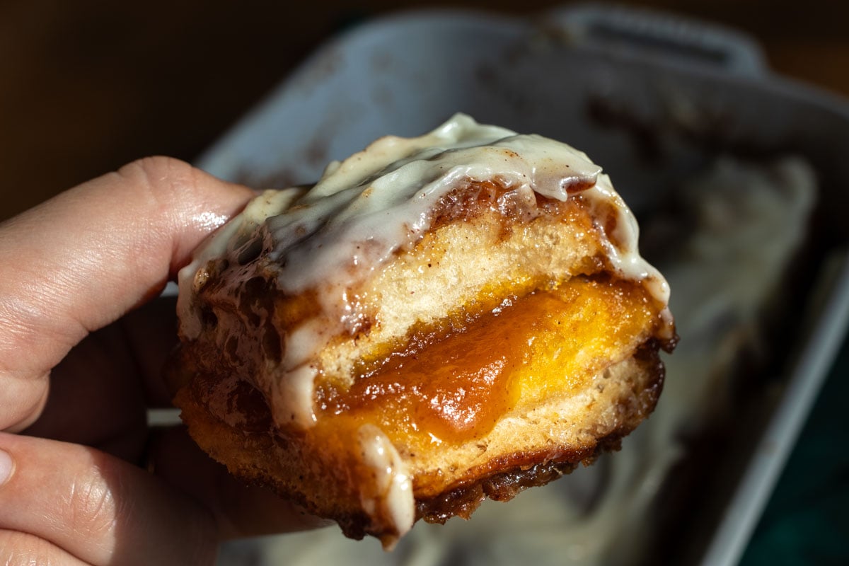 a hand holding a hawaiian roll turned cinnamon bun with cream cheese icing on top.