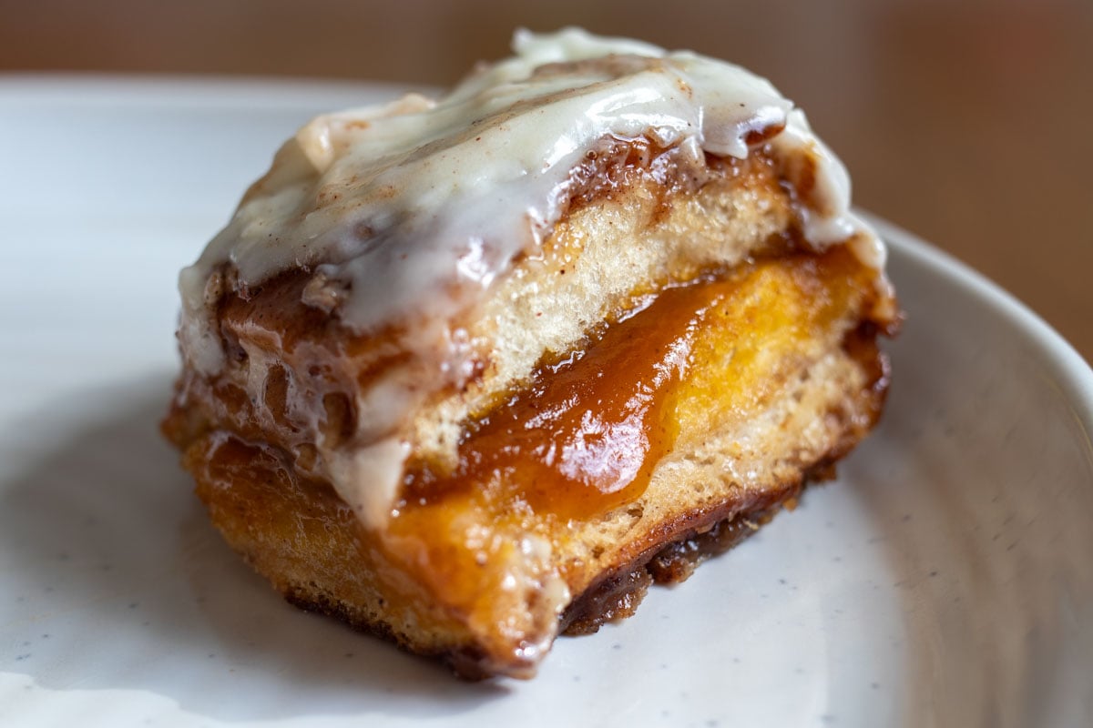 a white plate with a cinnamon roll on top of it with white icing dripping off.