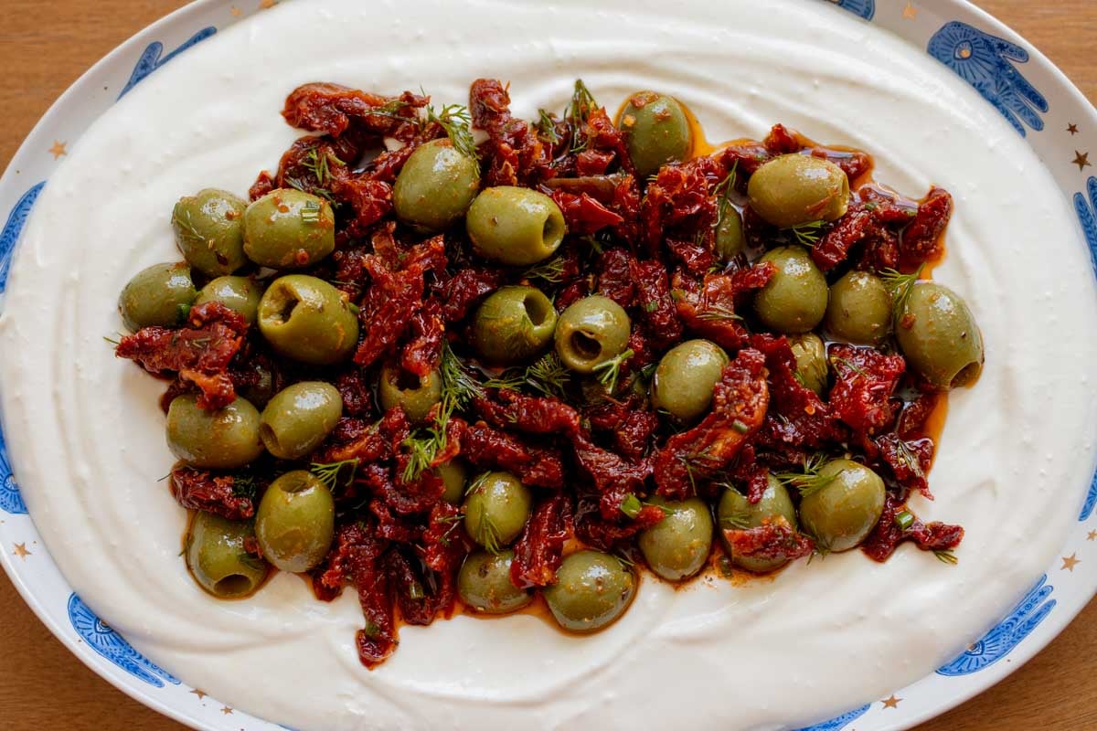 a close up of the texture of this colorful mediterranean dip with whipped feta yogurt, olives and tomatoes.